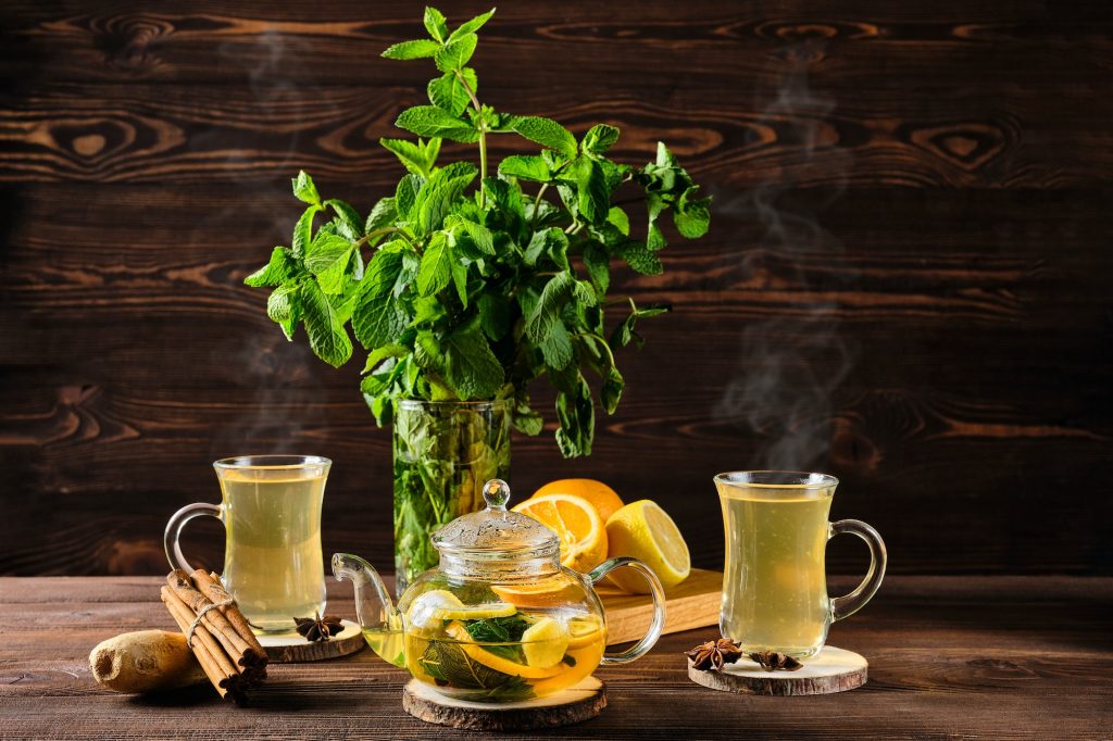 Citrus tea with ginger and mint leaves in a glass teapot, dark food photography.