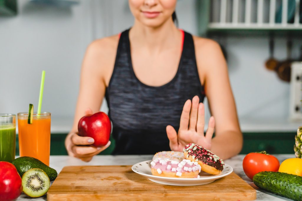 Young fit girl refuses eating doughnuts and opts for healthy food in the kitchen